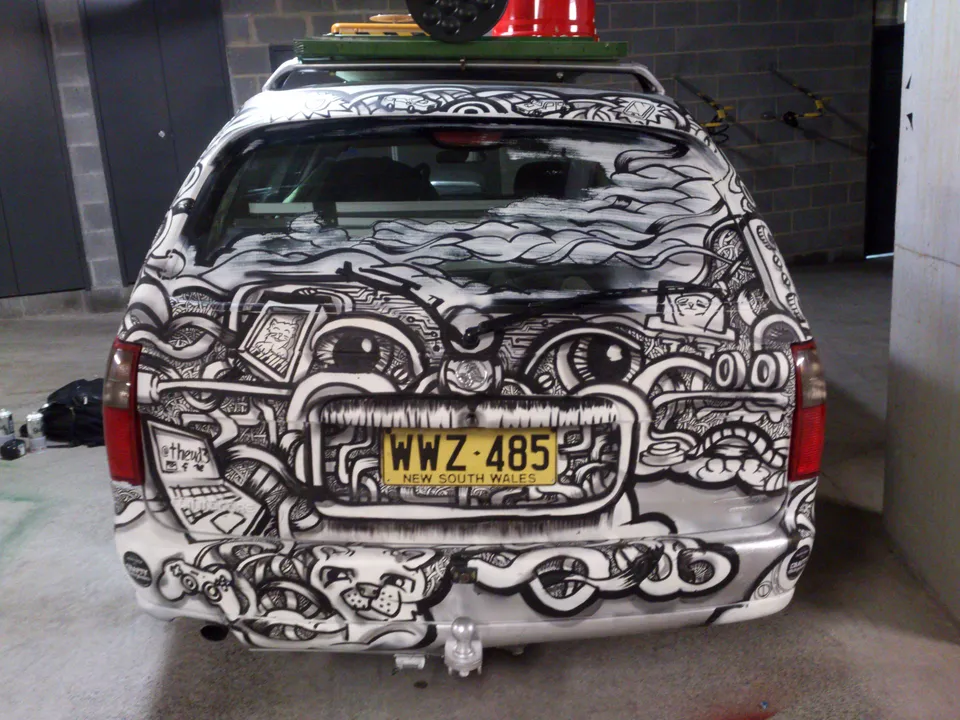 Rear of a station wagon hand-painted with bold black and white line art featuring psychedelic eyes and clouds