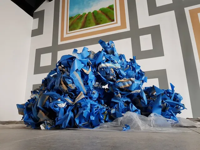 Pile of crumpled blue painter's tape on the floor beneath a partially painted geometric wall mural