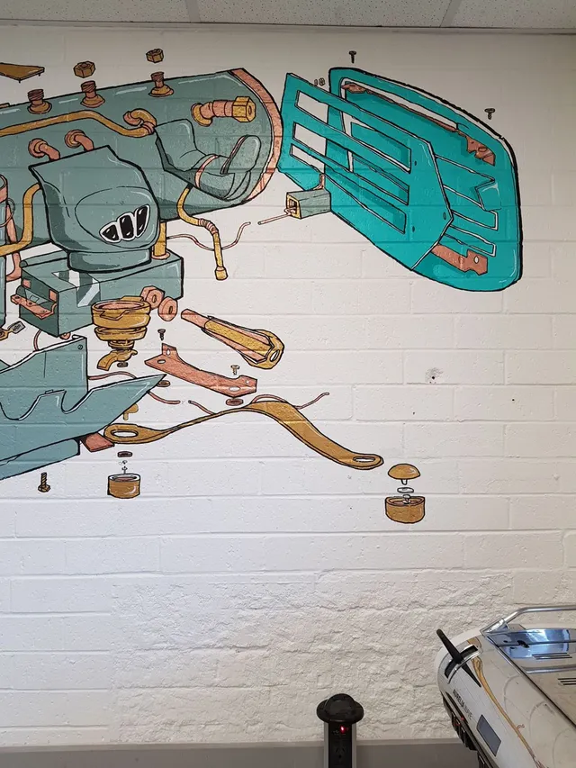 Mural on white brick showing an exploded diagram of espresso machine components painted in teal and copper