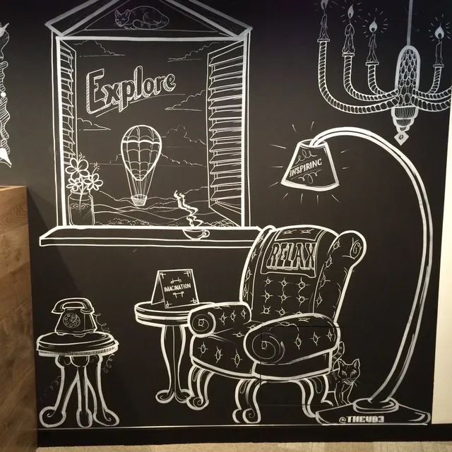 White line mural on a black wall showing an armchair, window with a hot air balloon, and the words Relax and Explore