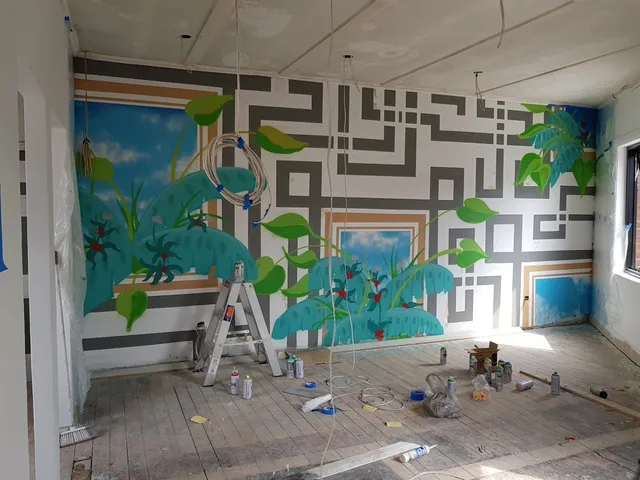 In-progress mural featuring a gray geometric maze, tropical plants, and painted windows showing a blue sky