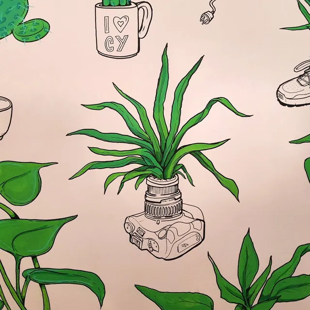 Mural detail of a green plant growing from an outlined camera lens, surrounded by leaves and other sketched objects