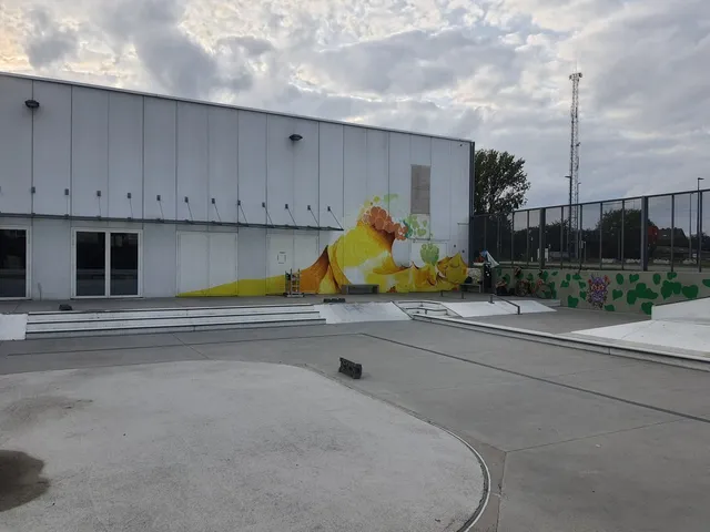 Large yellow and orange wave mural painted on a white building exterior at an outdoor concrete skate park