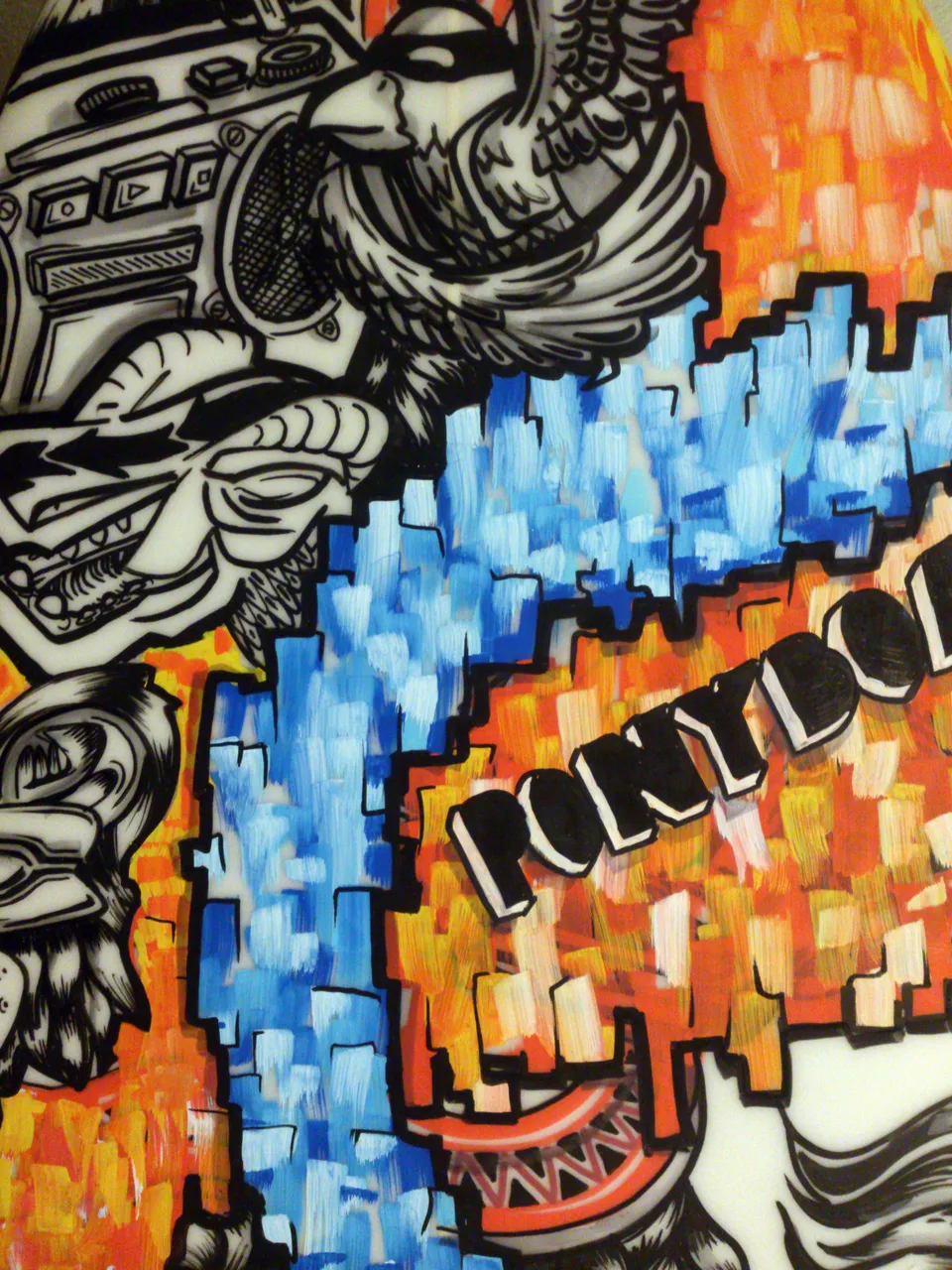 Painted surfboard detail with a black and white boombox and bird beside blocky blue and orange paint and the word PONYBOY