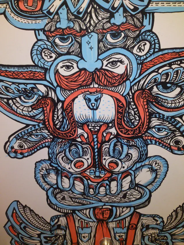 Psychedelic mural of a symmetrical totem with stacked faces, multiple eyes and snakes in bold blue, red and black lines