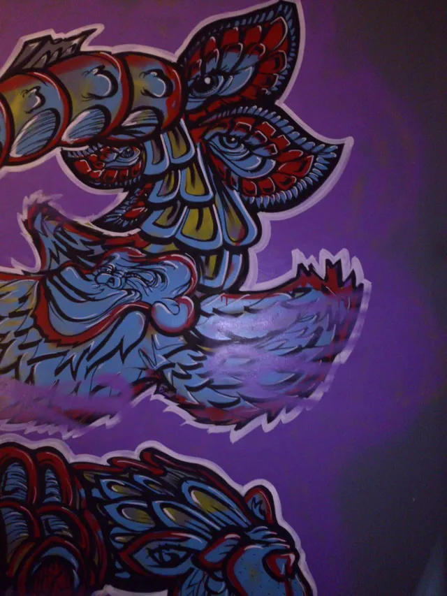 Psychedelic mural detail on a purple wall showing stylized blue and red totemic animal features with bold black outlines