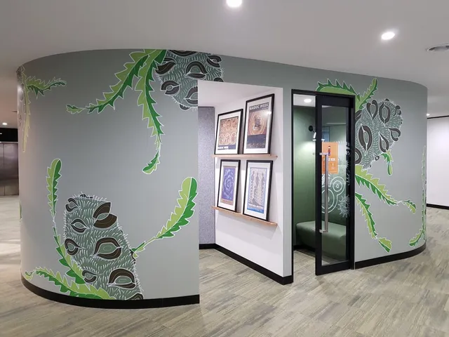 Mural of large stylized banksia seed pods and serrated green leaves on a curved gray office wall