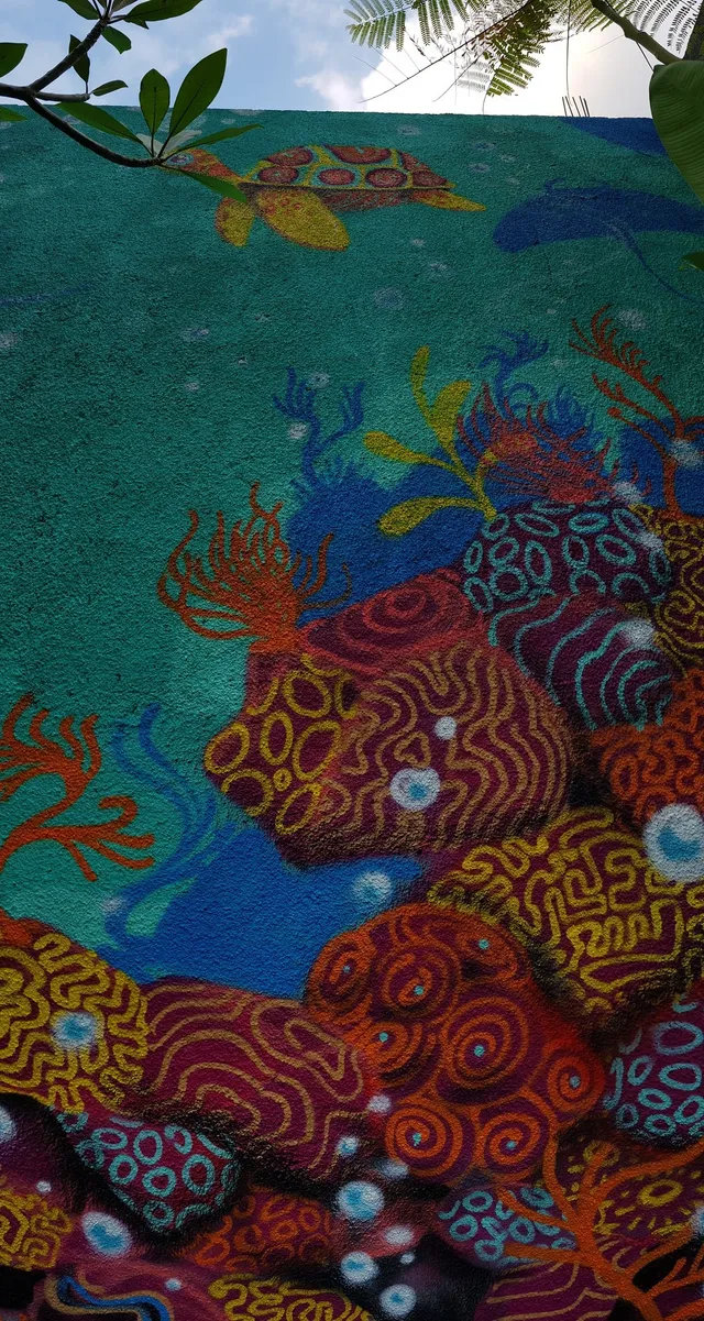 Textured outdoor mural of a sea turtle swimming above vibrant, psychedelic patterned coral