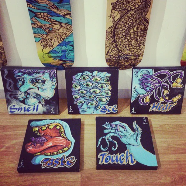Five psychedelic canvas paintings illustrating the five senses, arranged below two hand-painted skateboards