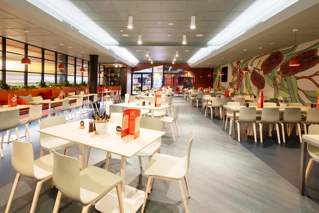 Restaurant interior featuring a large botanical wall mural depicting oversized red flowers and green leaves