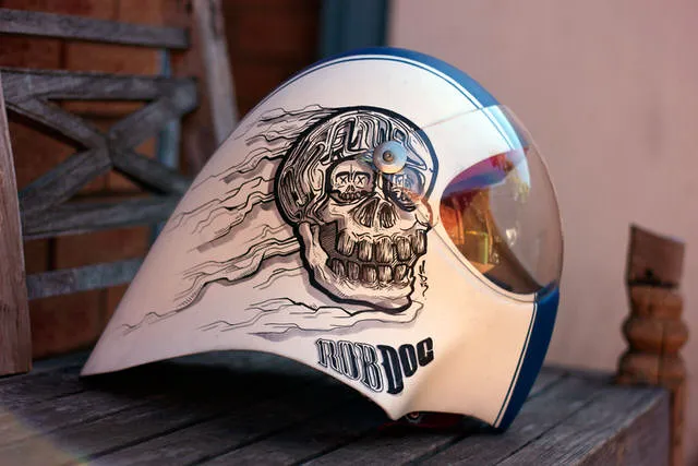 Hand-painted white helmet featuring a stylized skull with smaller skulls in its eyes and trailing speed lines