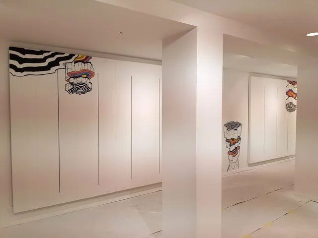 In-progress mural on white walls featuring stacked colorful cross-section shapes and bold black wavy lines