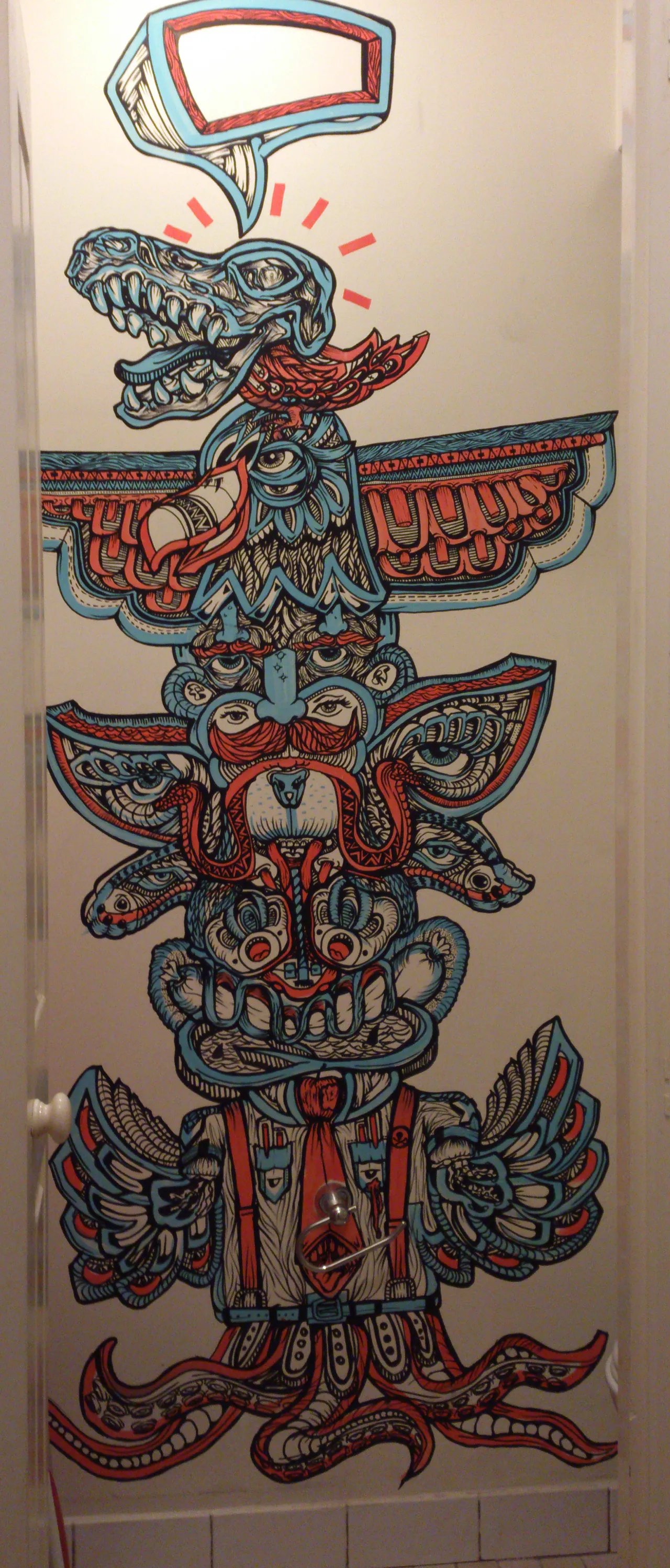 Mural of a psychedelic totem pole with stacked surreal faces, a skull, wings, and tentacles in bold red and blue