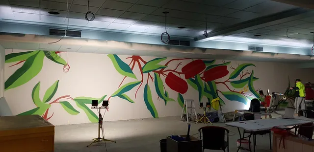 Indoor mural in progress featuring large stylized red flowers and green leaves on a wide white wall
