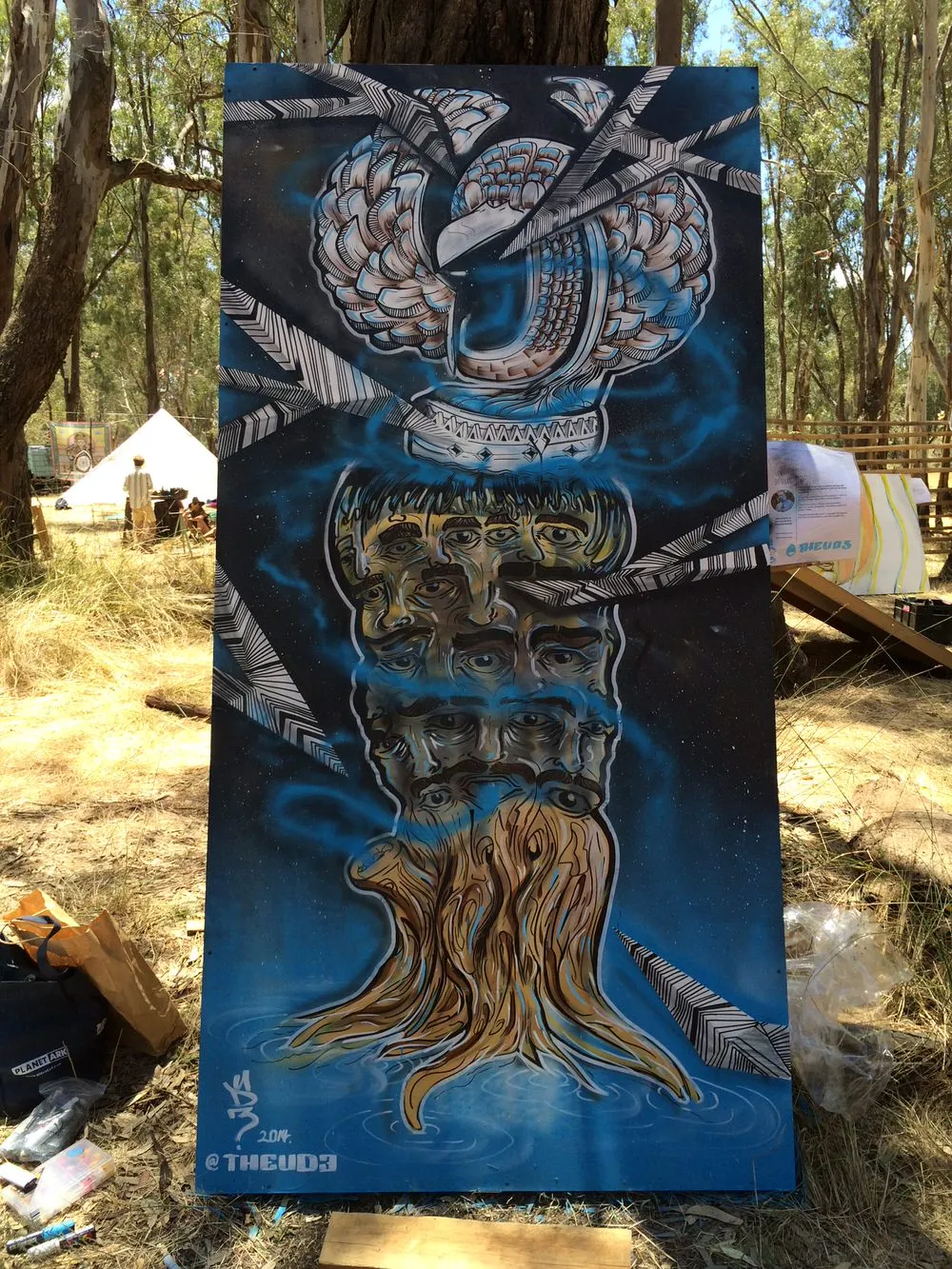 Mural panel of a psychedelic totem featuring twisting roots, stacked multi-eyed faces, a bird head, and geometric shards