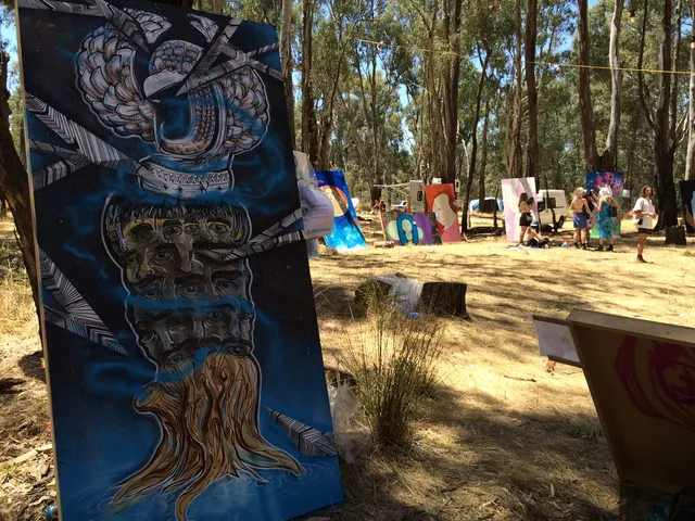 Live art painted panel outdoors depicting a psychedelic totem of stacked faces, multiple eyes, and roots
