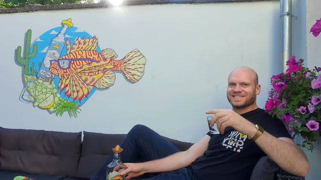 Wall mural of a vibrant lionfish wearing sunglasses next to a tequila bottle, with a man sitting on a sofa in front