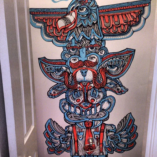 Red and blue mural on a door depicting a psychedelic totem pole with an eagle, multiple eyes, and a bearded face