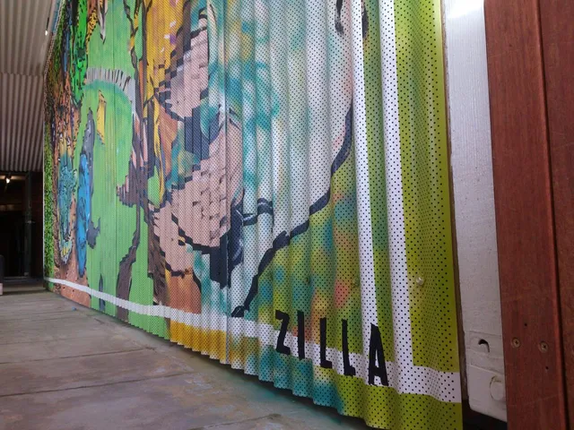 Colorful mural on a corrugated metal surface featuring abstract animal forms and the painted word ZILLA at the bottom