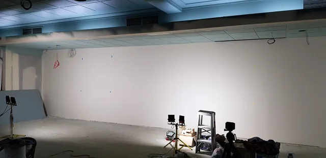 Large blank white wall prepared for a mural with work lights, a stepladder, and painting supplies