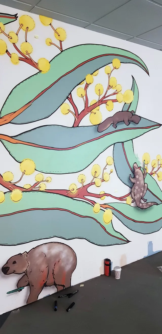 In-progress wall mural of giant eucalyptus leaves, yellow wattle flowers, a wombat, a platypus and a lizard