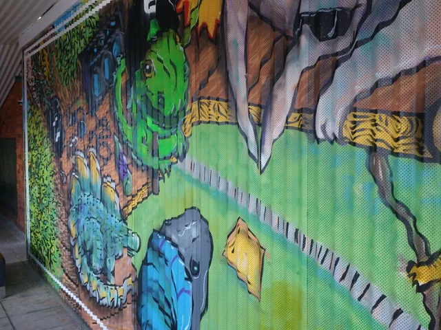 Mural on corrugated metal depicting a stylized green monster and large grey hands gripping a yellow wooden structure