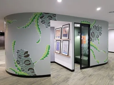 Interior mural of large stylized banksia pods and jagged green leaves on a curved grey wall