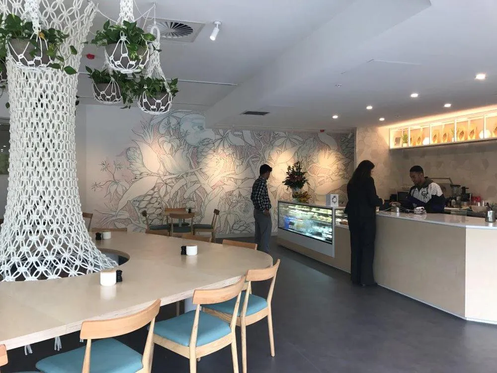 Botanical line-drawing mural across the walls of an NRMA café, with seating and a service counter.