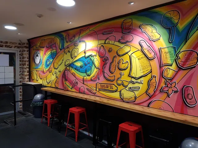 Indoor mural of floating cartoon food and objects on a swirling rainbow background behind a counter with red stools