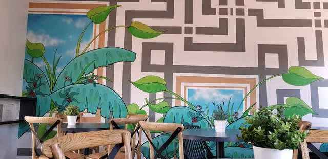 Cafe mural depicting bold green tropical plants and grey geometric maze patterns around painted blue sky panels