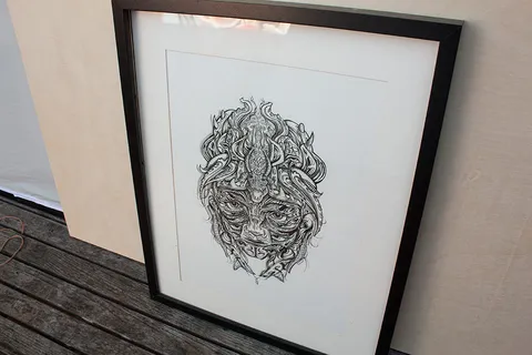 Framed ink drawing of a highly detailed, symmetrical crocodile mask with intricate line work