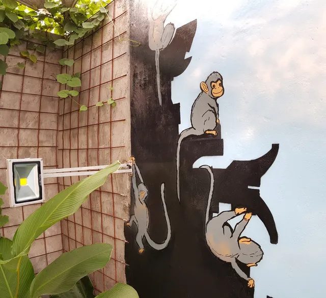 Mural of three grey monkeys climbing on a black tiered temple silhouette against a light blue painted sky