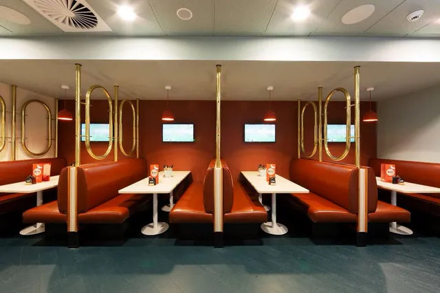 Restaurant interior with red leather booths, white tables, and brass oval partitions lining a dark red wall
