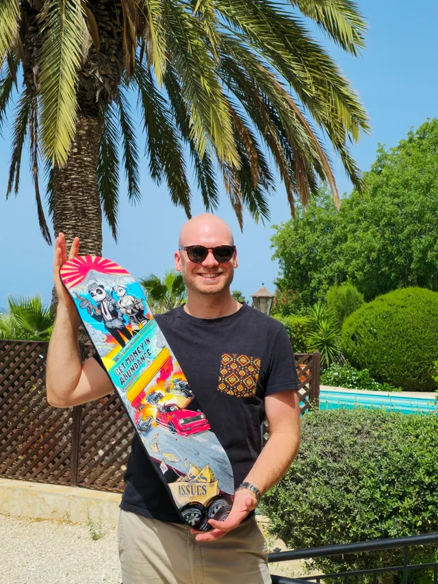 Man holding a painted skateboard featuring an armed panda, a car chase, and the phrase Get Money in Abundance