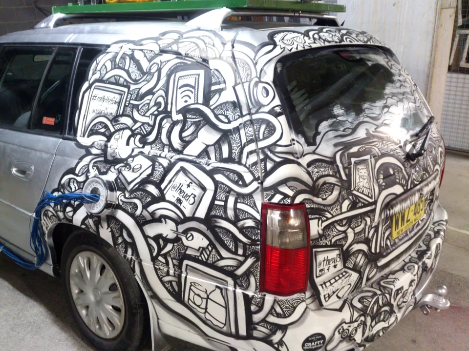 Silver station wagon with a hand-painted black and white mural of tangled cables and bold line work covering its rear half
