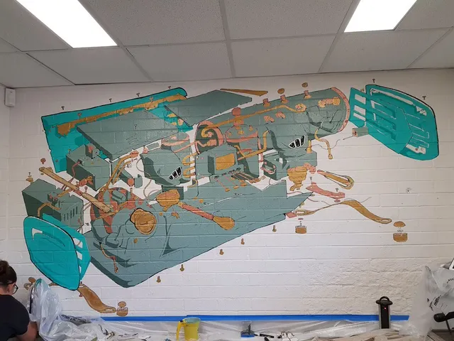 Indoor mural on a white brick wall showing an exploded diagram of a teal and copper espresso machine