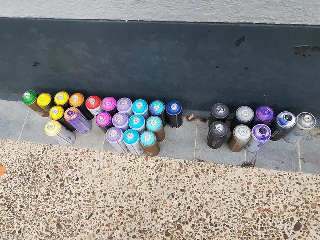 Row of colorful spray paint cans lined up on the pavement against a dark wall