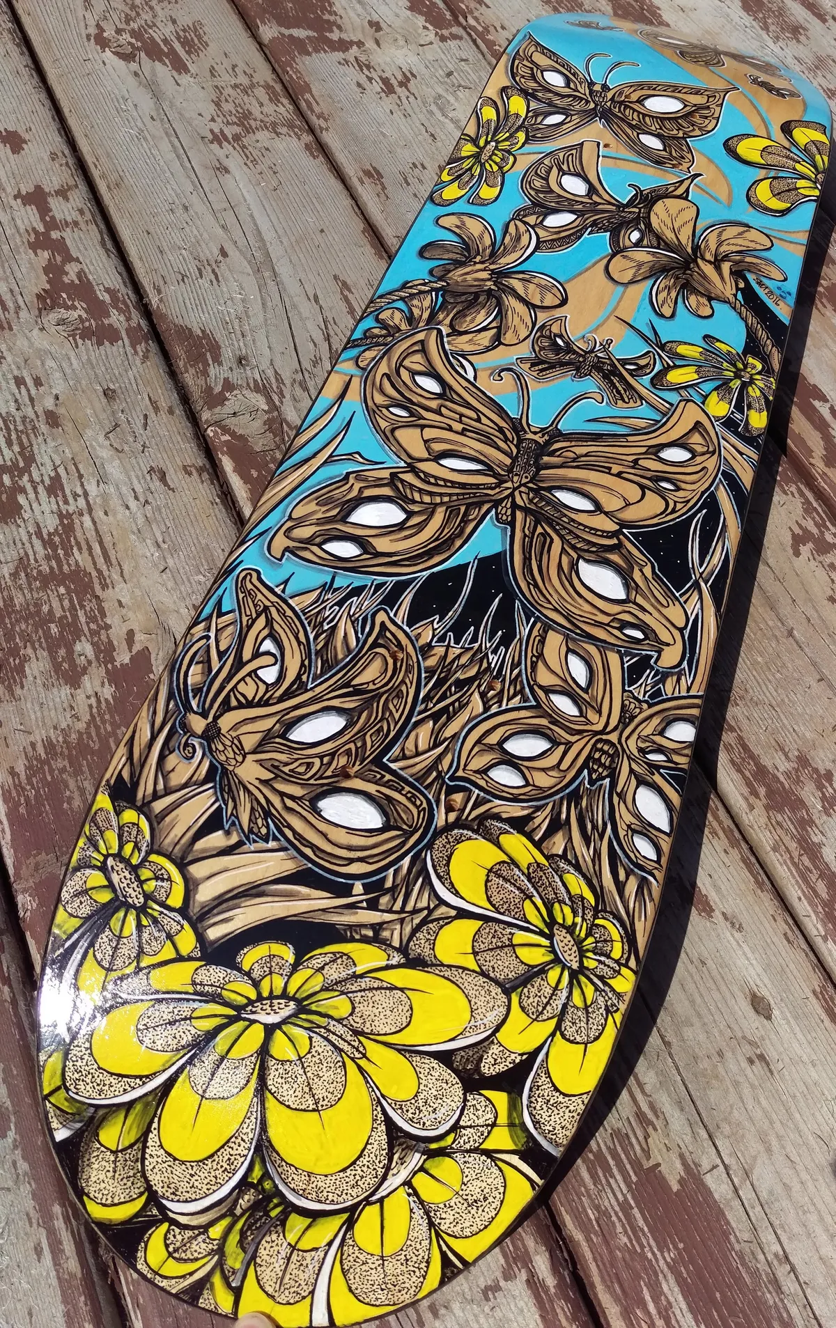 Painted skateboard deck featuring brown moths and large yellow flowers with bold black outlines