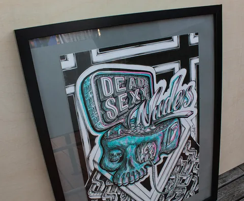 Framed illustration of a stylized open skull emitting a sign reading DEAD SEXY Nudes in cyan and pink