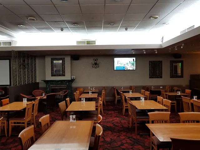 Empty restaurant dining room with wooden tables, chairs, and a red patterned carpet
