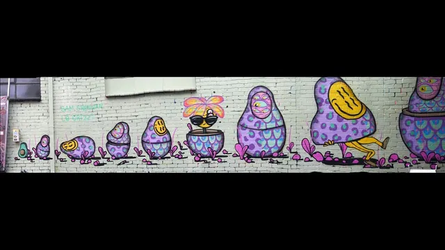 Brick wall mural depicting a row of psychedelic purple babushka dolls with smiley faces, multiple eyes, and legs