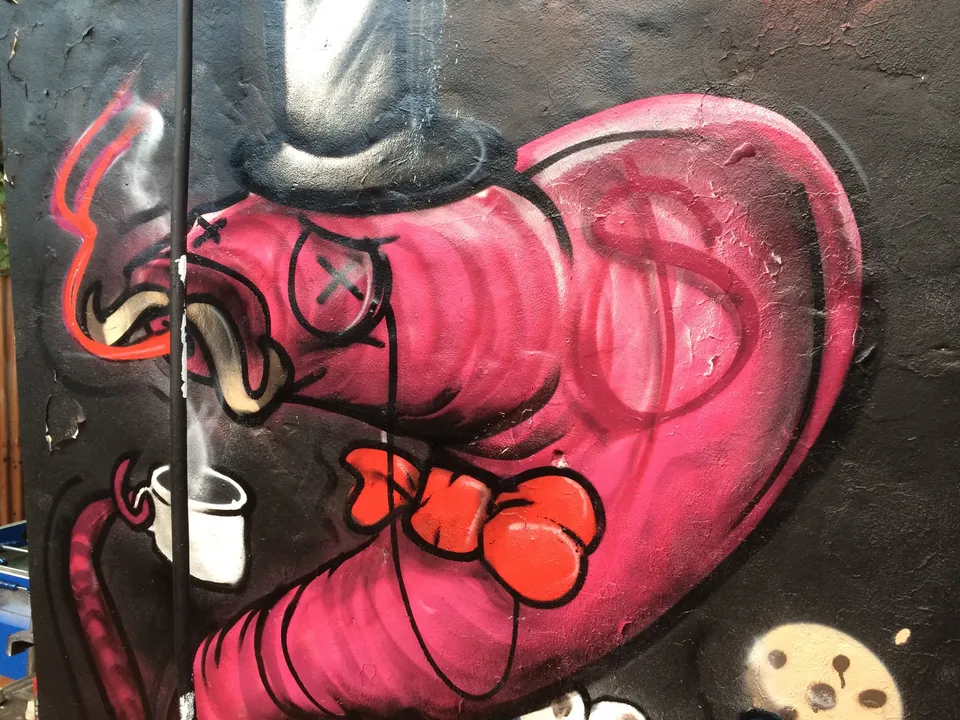 Graffiti mural: pink worm in top hat & monocle with dollar sign, constricting blue Cookie Monster holding a cookie