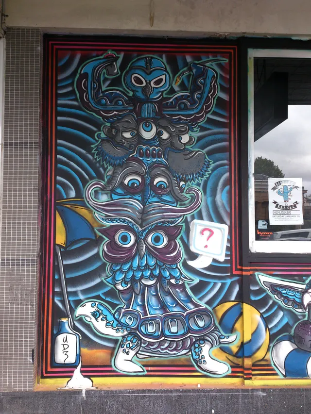 Mural of a psychedelic blue totem with stacked animal faces and a speech bubble containing a red question mark