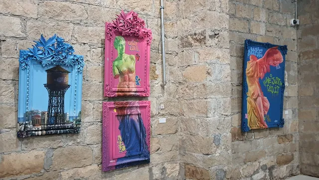 Brightly painted, ornate frames on a stone wall displaying mixed media art of classical statues and a water tower
