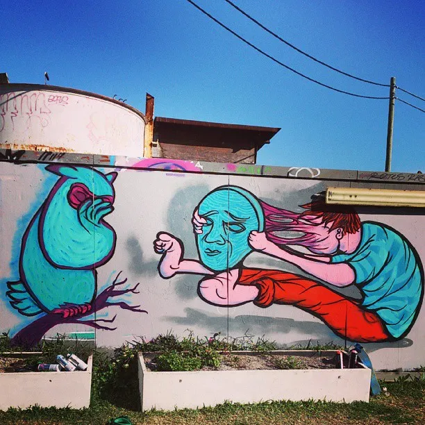 Mural of a surreal blue bird and a figure whose face stretches forward into a large blue mask