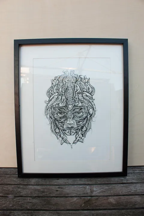 Framed ink drawing of a highly detailed, symmetrical crocodile mask featuring multiple eyes and intricate linework