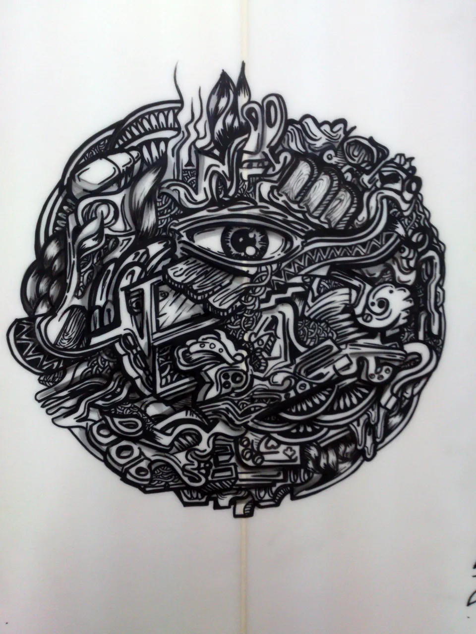 Circular psychedelic black ink drawing on a surfboard featuring a large central eye and intricate abstract patterns