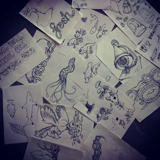 Scattered loose paper scraps with black ink sketches of animals, surreal shapes, and stylized lettering