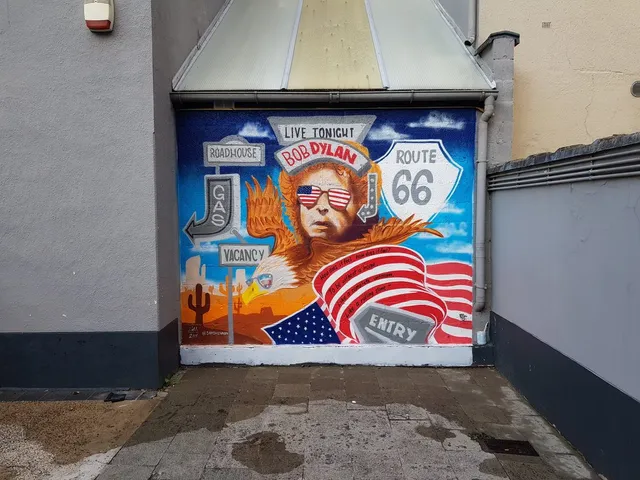 Exterior mural depicting Bob Dylan in American flag sunglasses, an eagle, a Route 66 sign, and a desert landscape