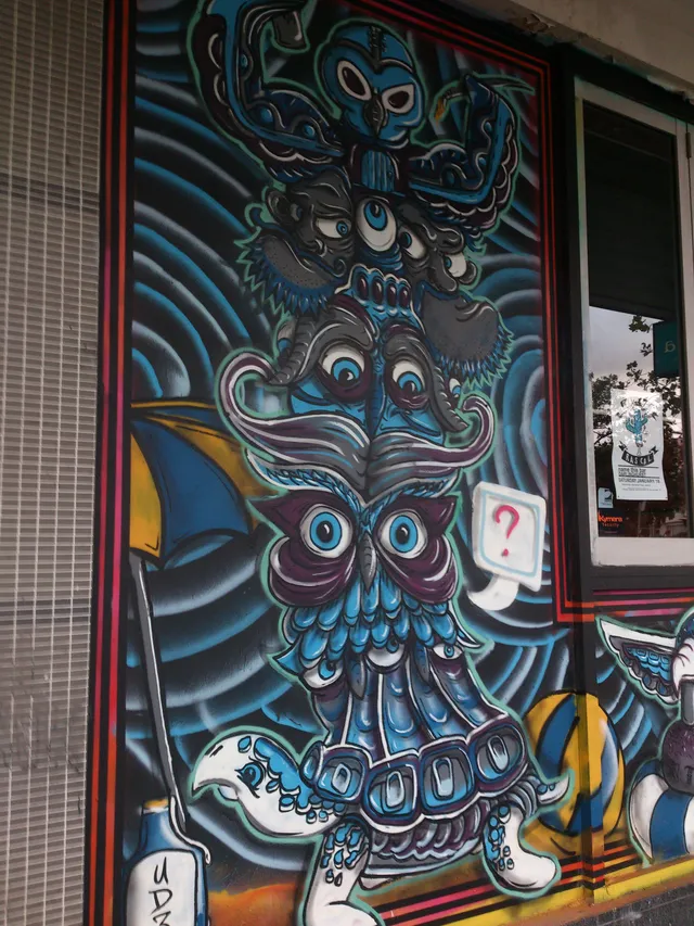 Mural of a psychedelic totem stack of blue animal faces, anchored by an owl beside a question mark speech bubble